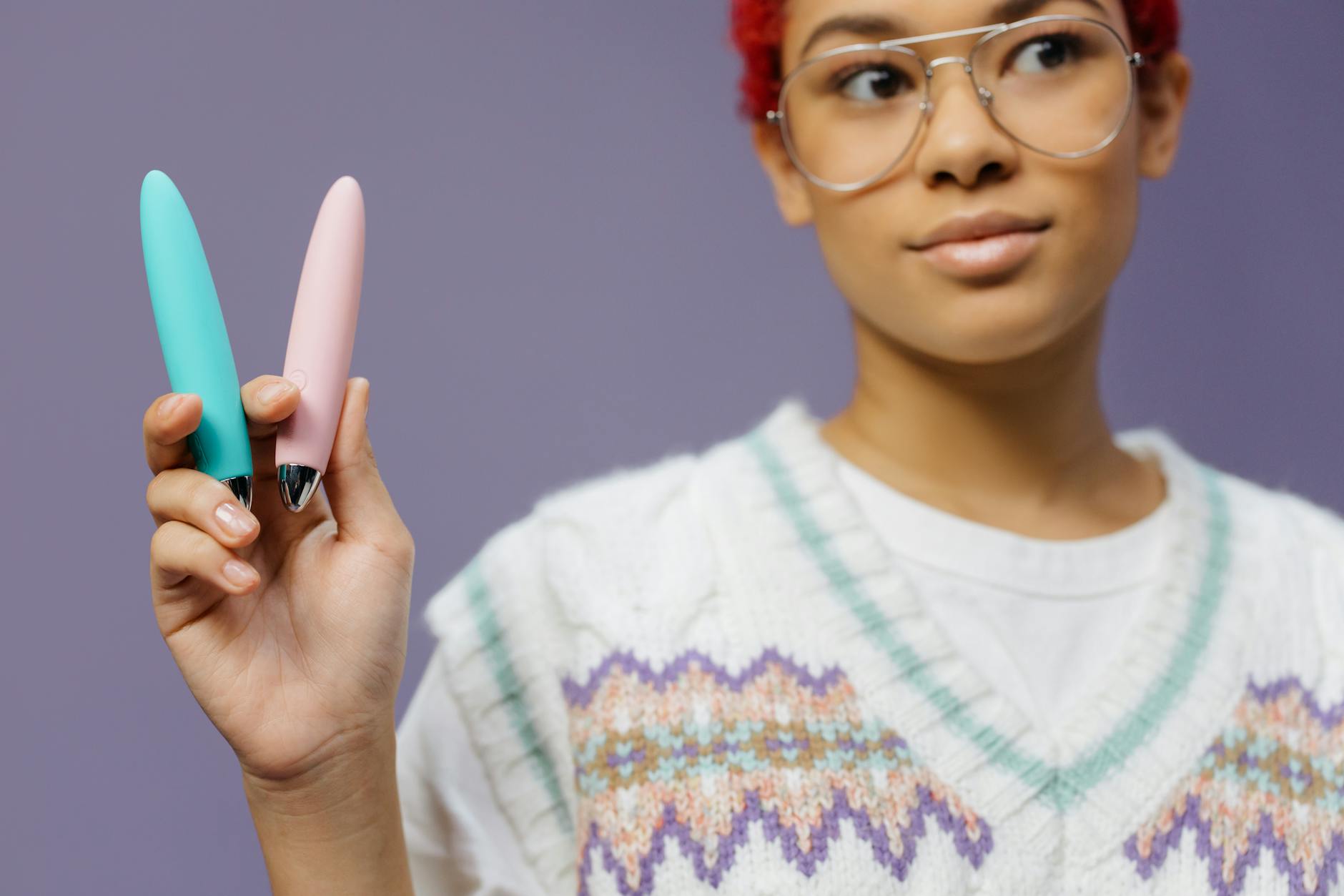A hand holding a vibrator against a minimalistic purple backdrop